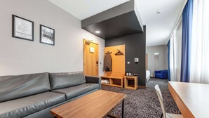 A modern hotel room with a grey sofa, wooden coffee table, and a patterned carpet.