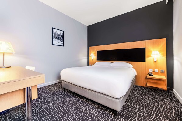 Una habitación de hotel con cama, mesitas de noche, escritorio y alfombra estampada.