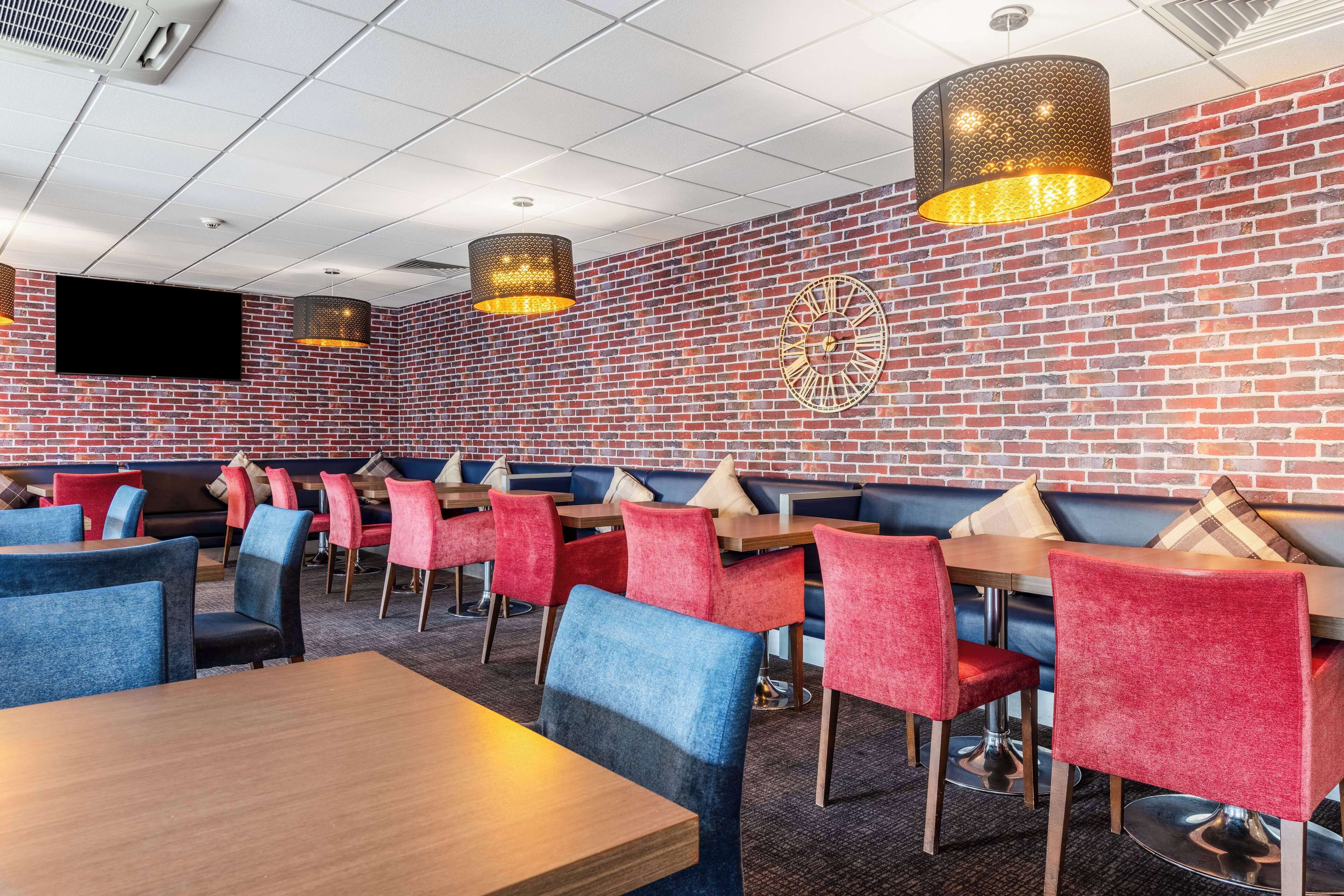 Un restaurante con paredes de ladrillo, sillas rojas y azules, mesas de madera y lámparas colgantes.