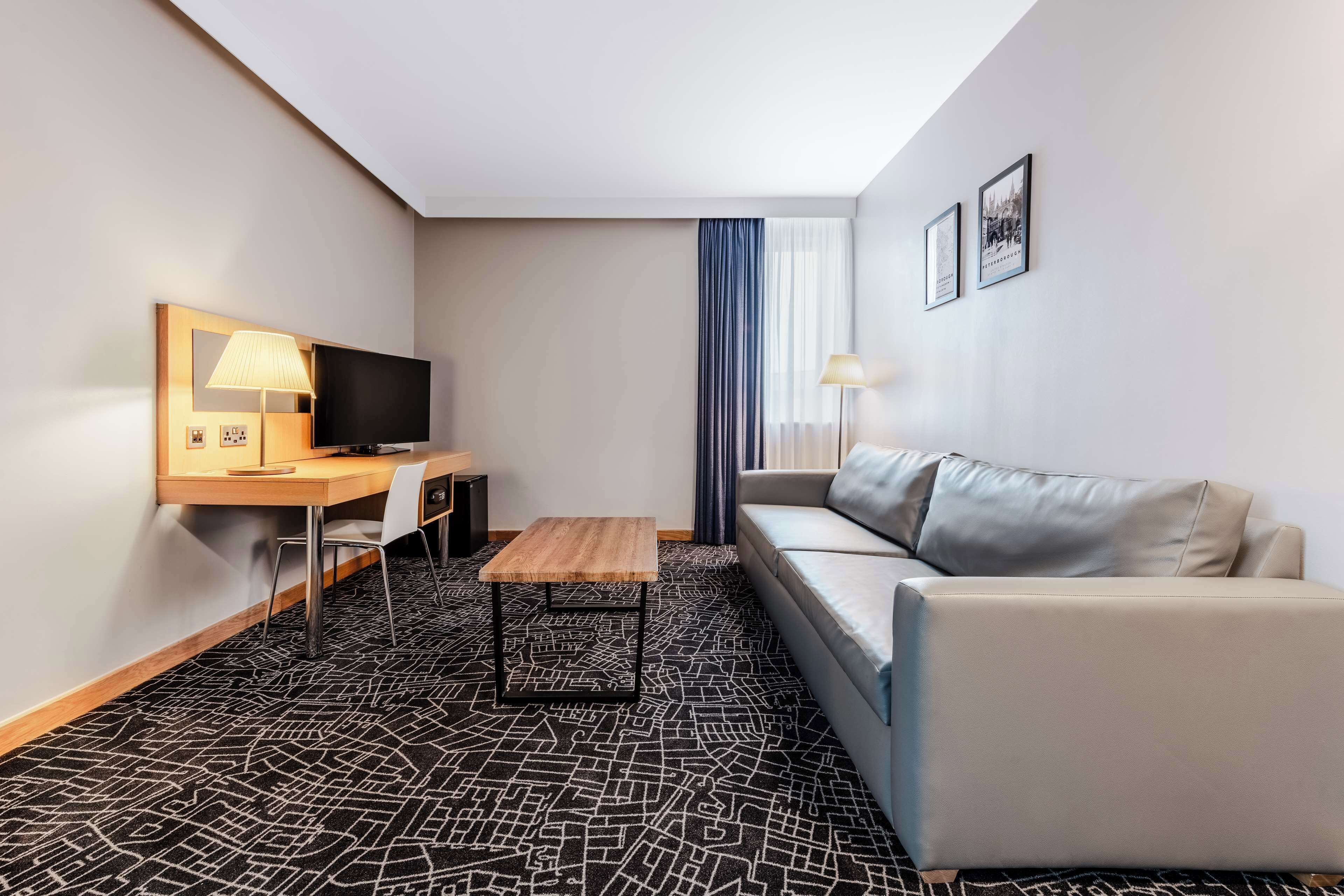 A hotel room with a sofa, a TV, a desk, and a patterned carpet.