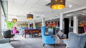 A modern lobby with a pool table, comfortable seating, and a bar area.