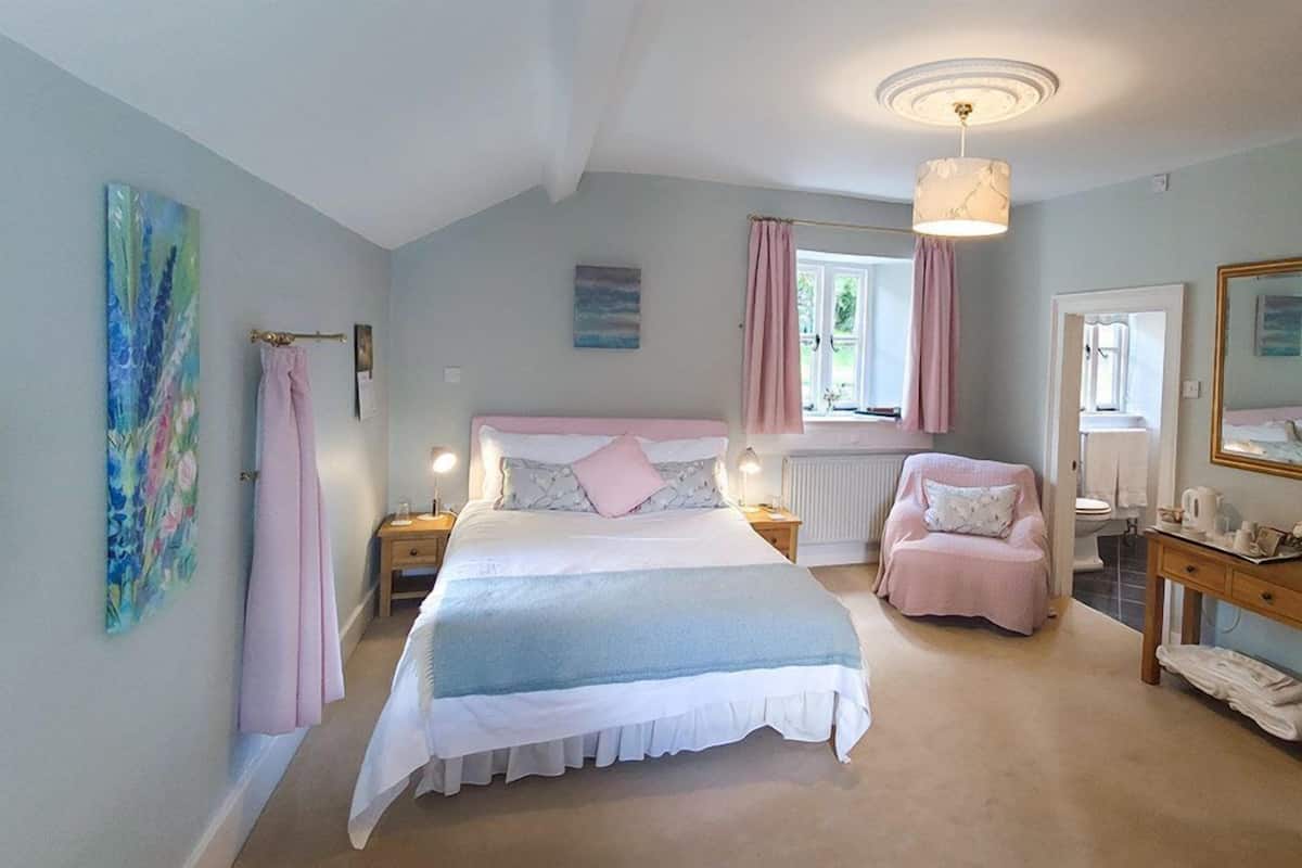 Une chambre à coucher avec un lit, des tables de chevet, une chaise, une fenêtre avec des rideaux et un tableau au mur.