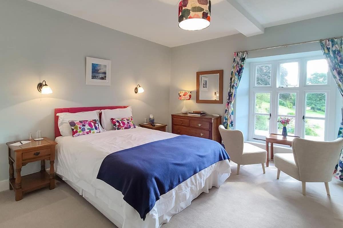 Une chambre à coucher avec un grand lit, des tables de chevet, une commode, une chaise et une fenêtre avec des rideaux.