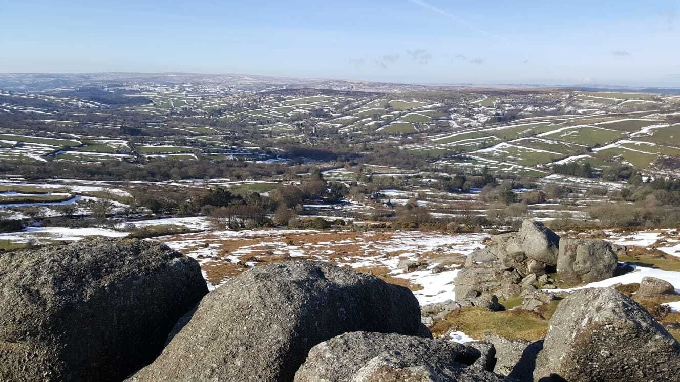 A panoramic view of a rural landscape with rolling fields and scattered rocks.