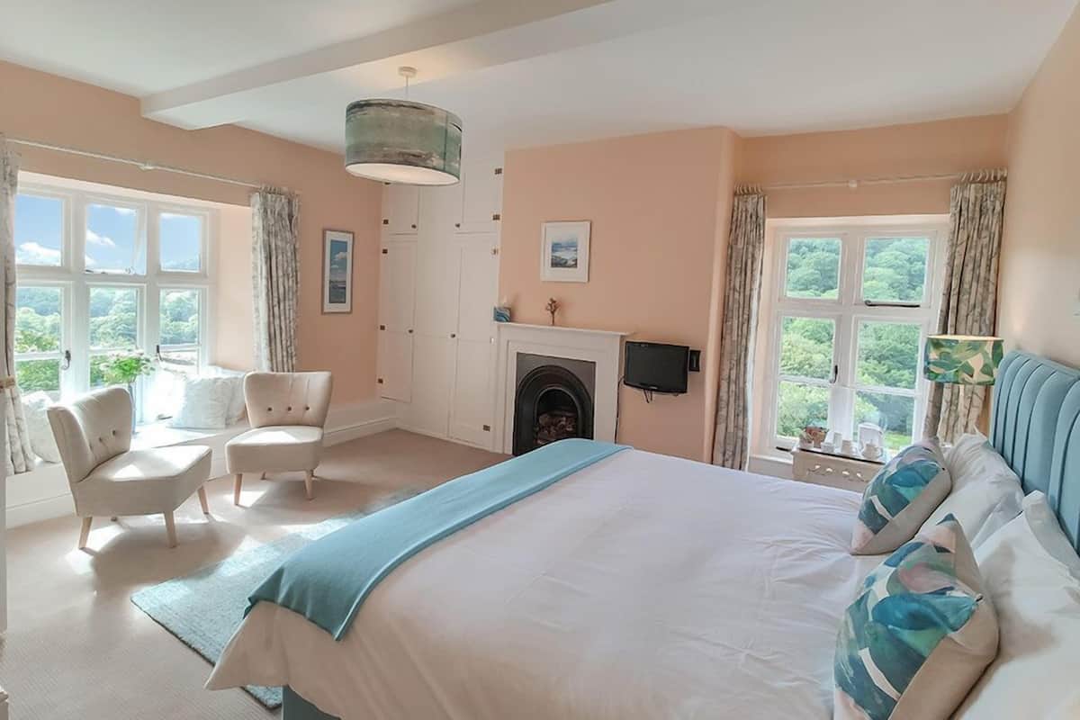 Une chambre avec un grand lit, deux fauteuils, une cheminée et un téléviseur.