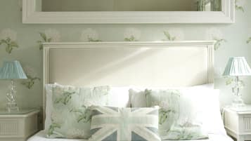 A neatly made bed with floral pillows and a white headboard. There are two bedside tables with lamps.