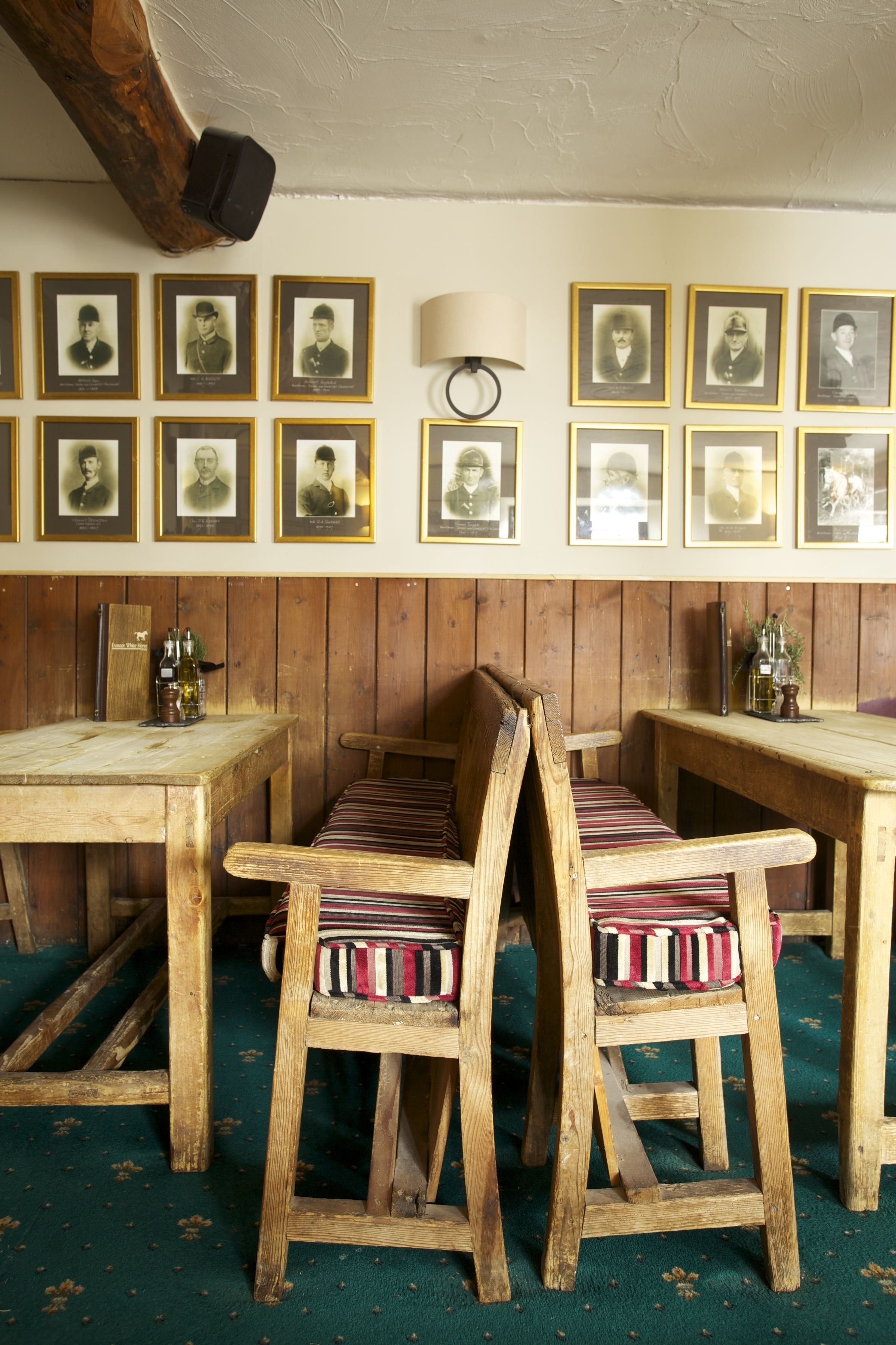 A rustic room with wooden furniture, framed portraits on the wall, and a green carpet.