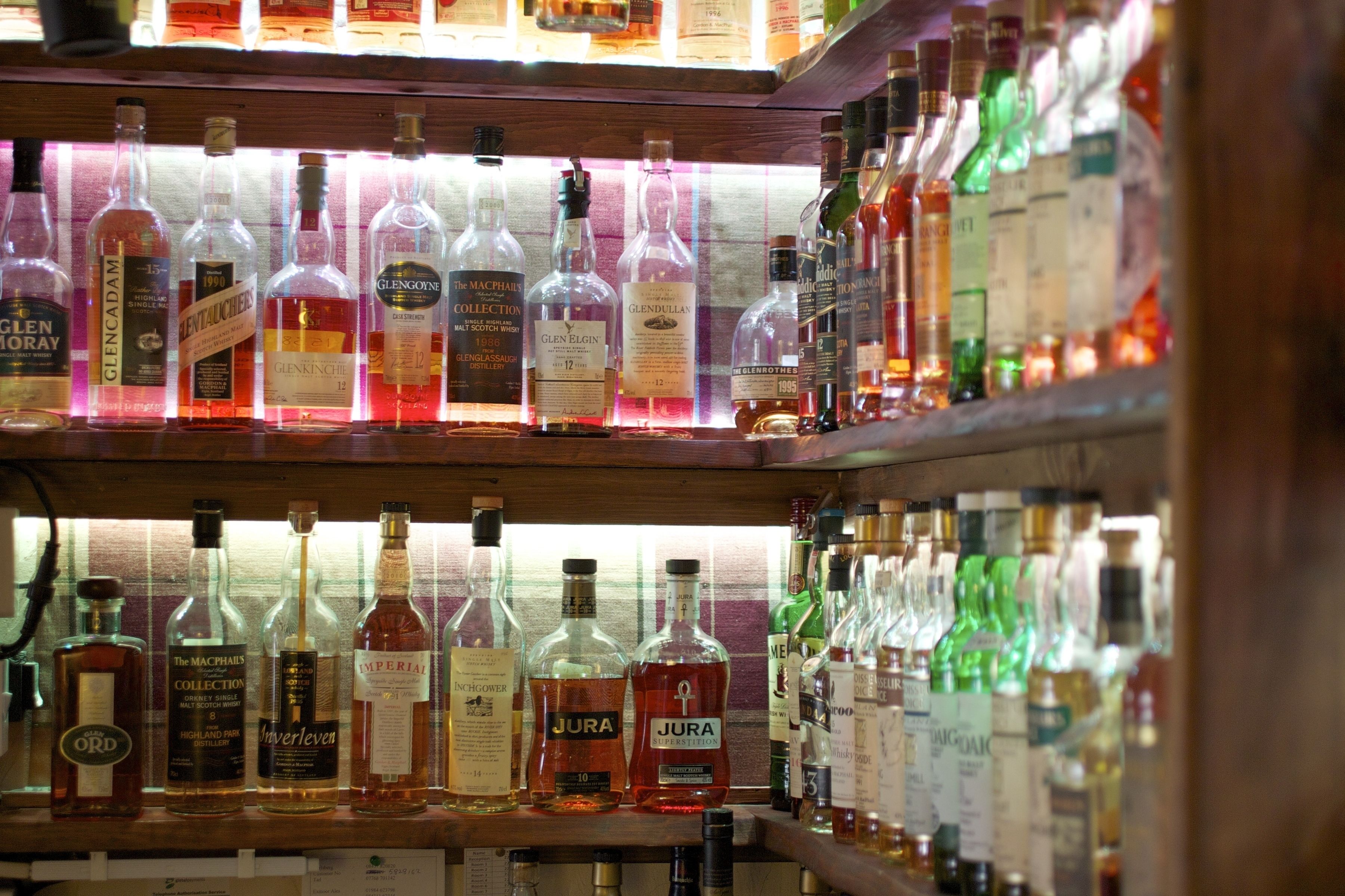 Des étagères remplies de bouteilles de différentes sortes de spiritueux, notamment des marques comme Glenfiddich et JURA.