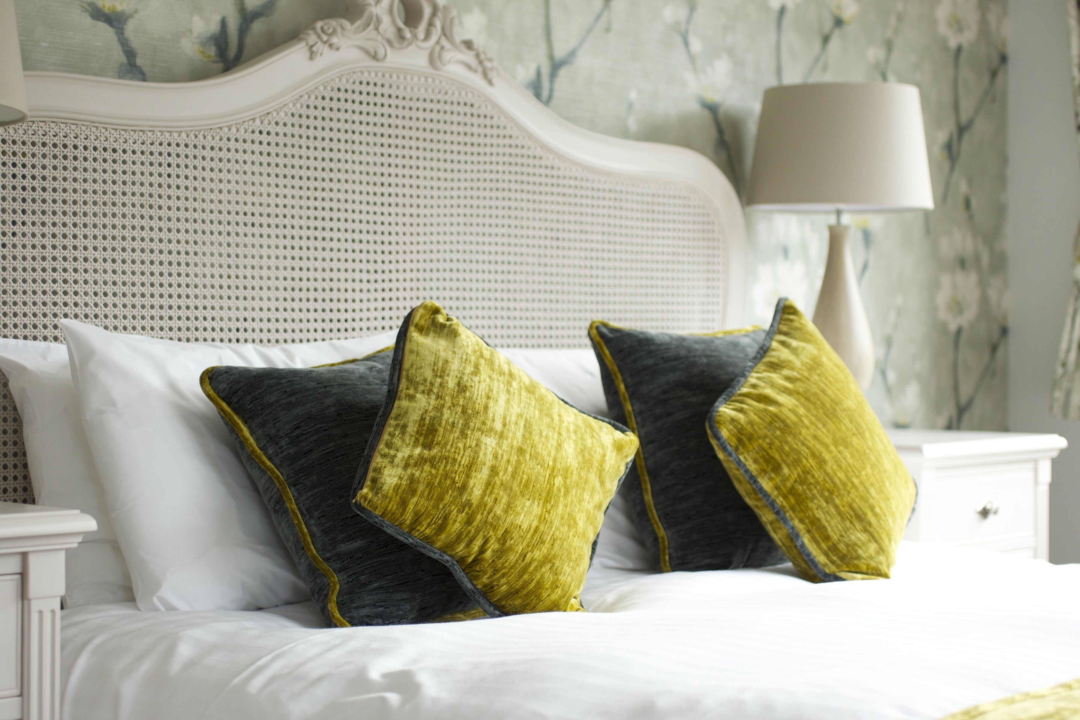 A bed with white bedding and two pillows, one dark and one yellow, in a room with a white headboard and a lamp on a nightstand.