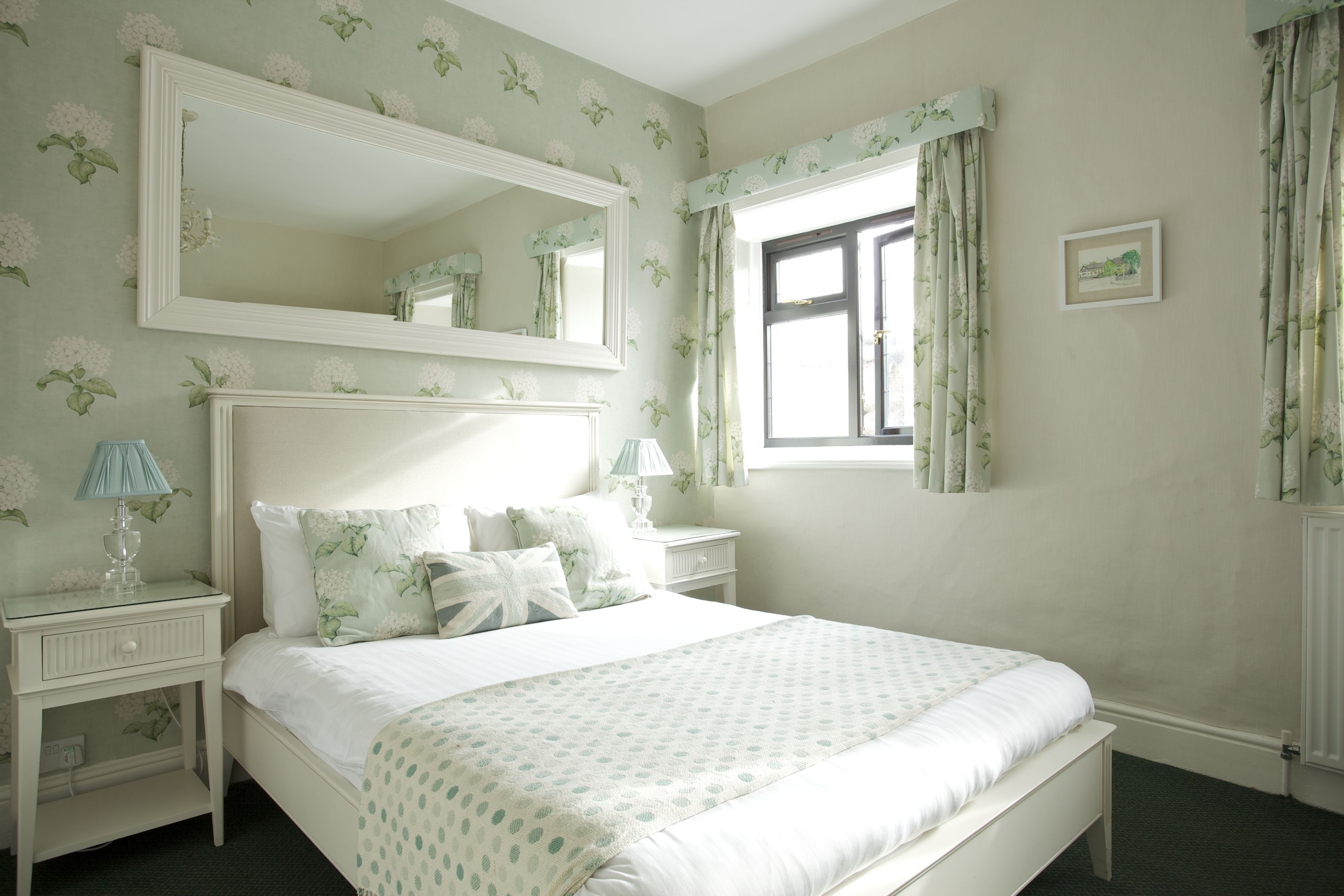 A bedroom with a large bed, a nightstand, a dresser, a mirror, and a window with curtains.