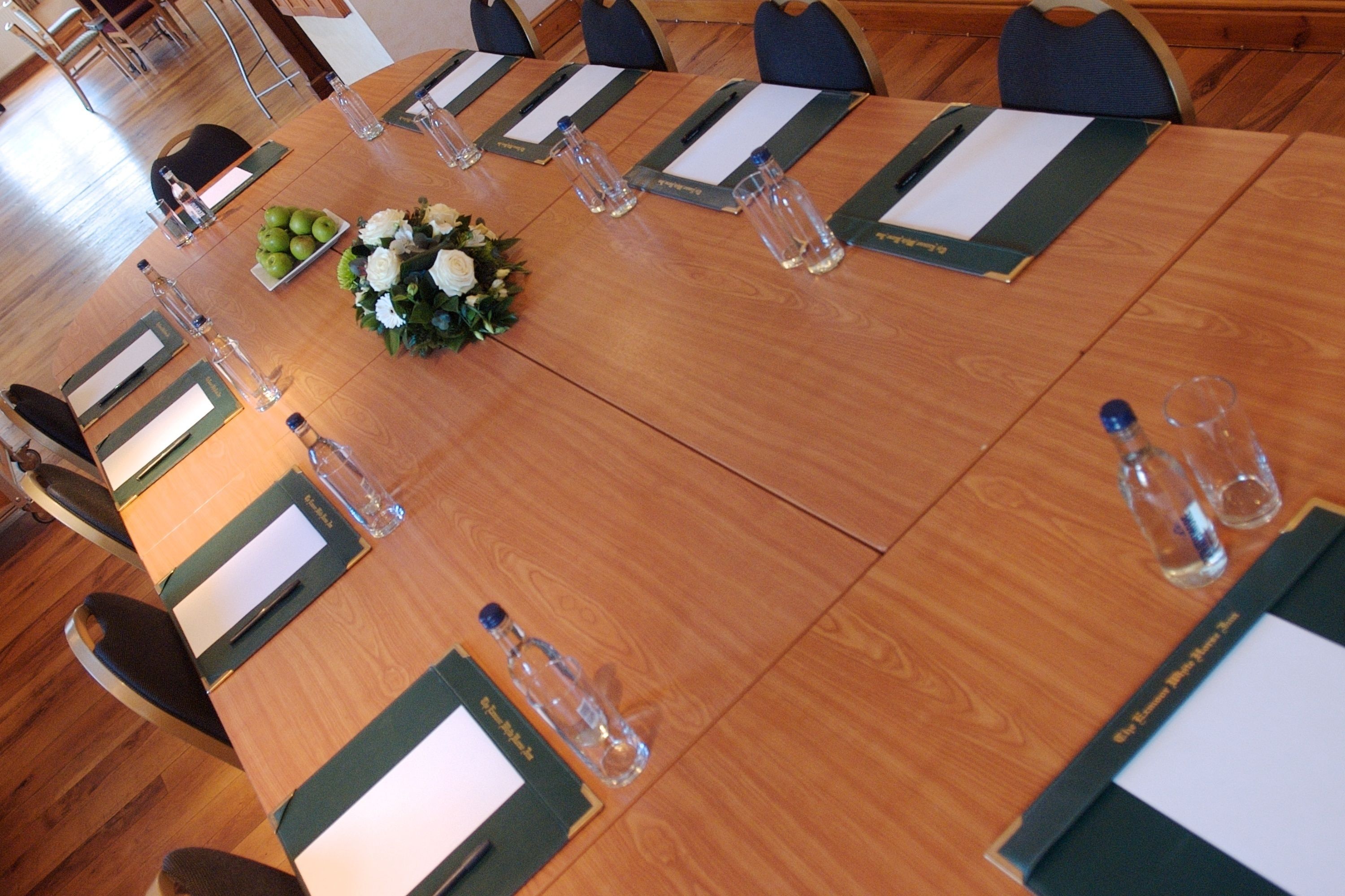 A conference room with a long table, chairs, water bottles, and a floral centerpiece.