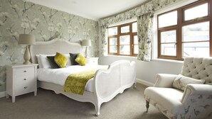 A bedroom with a white bed, a nightstand, a chair, and a window with floral curtains. - Exmoor White Horse Inn (Minehead)