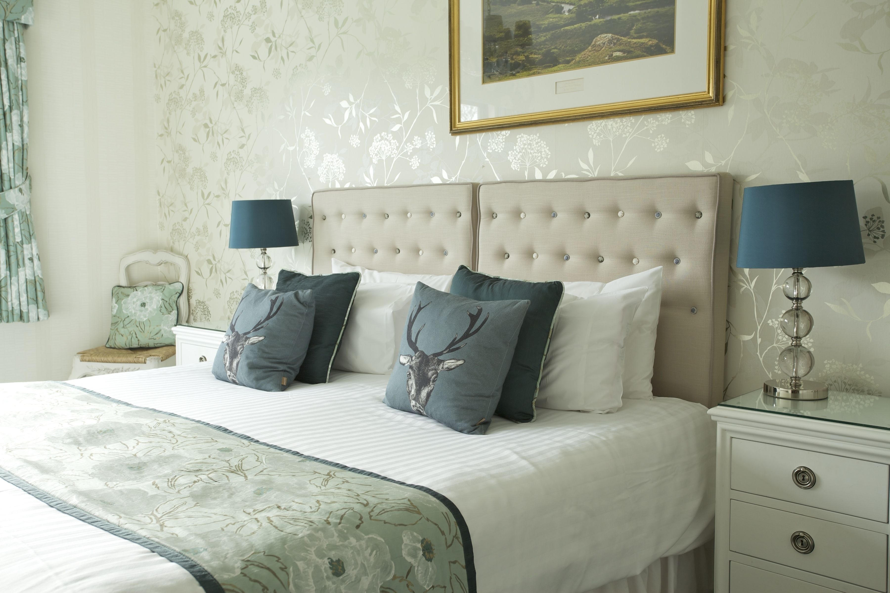 A neatly made bed with a floral bedspread, two bedside lamps, and a framed picture on the wall.