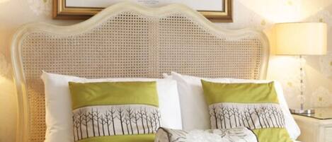 A bed with a woven headboard, two green pillows with tree designs, and a white pillow with a floral pattern.