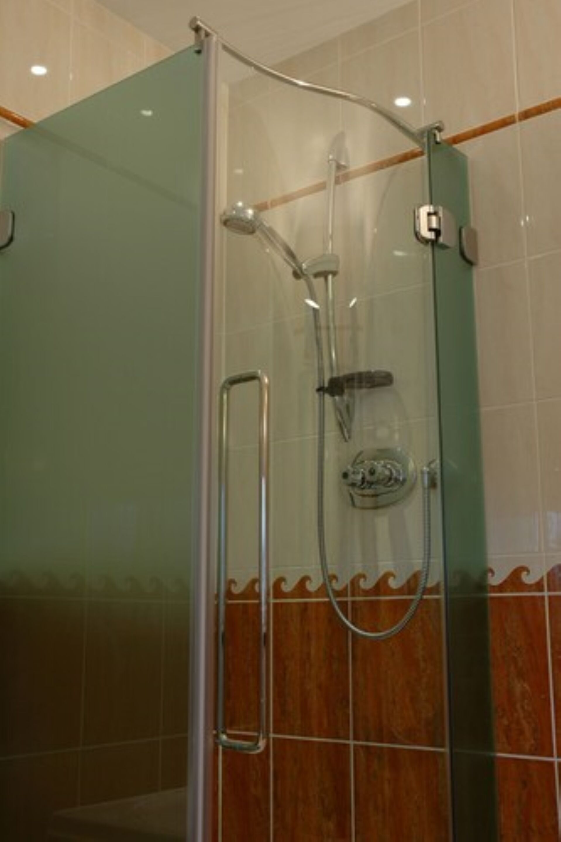 A glass-enclosed shower with a handheld showerhead and a wall-mounted faucet.