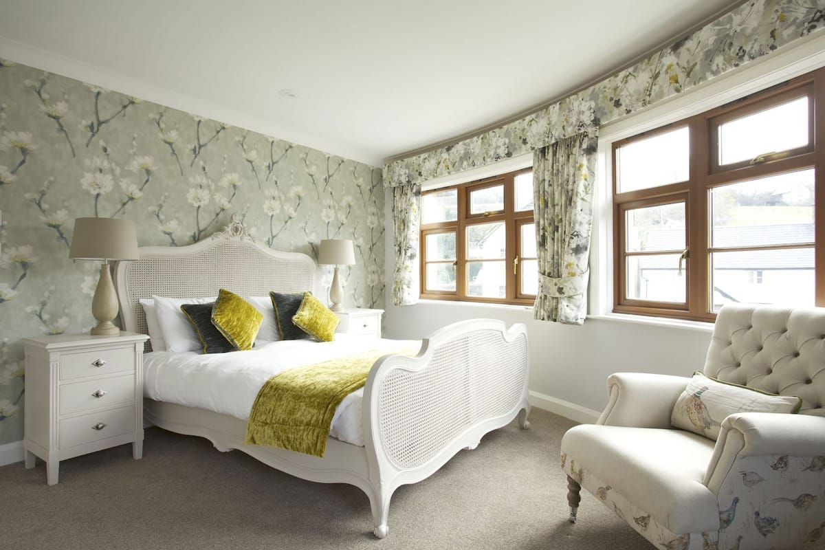 A bedroom with a bed, nightstands, a chair, and large windows.