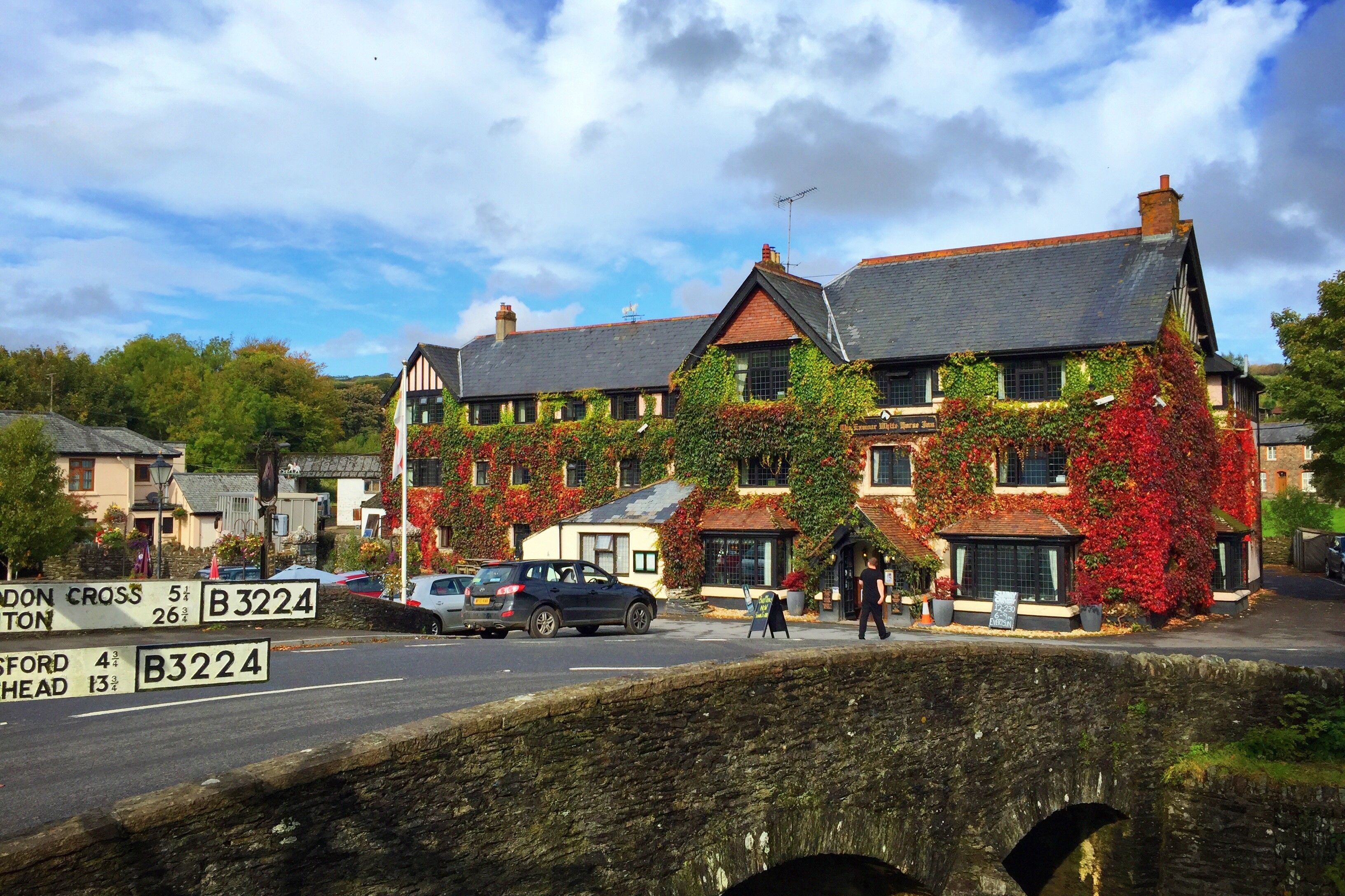 A traditional building with ivy-covered walls, a stone bridge in the foreground, and a clear sky.