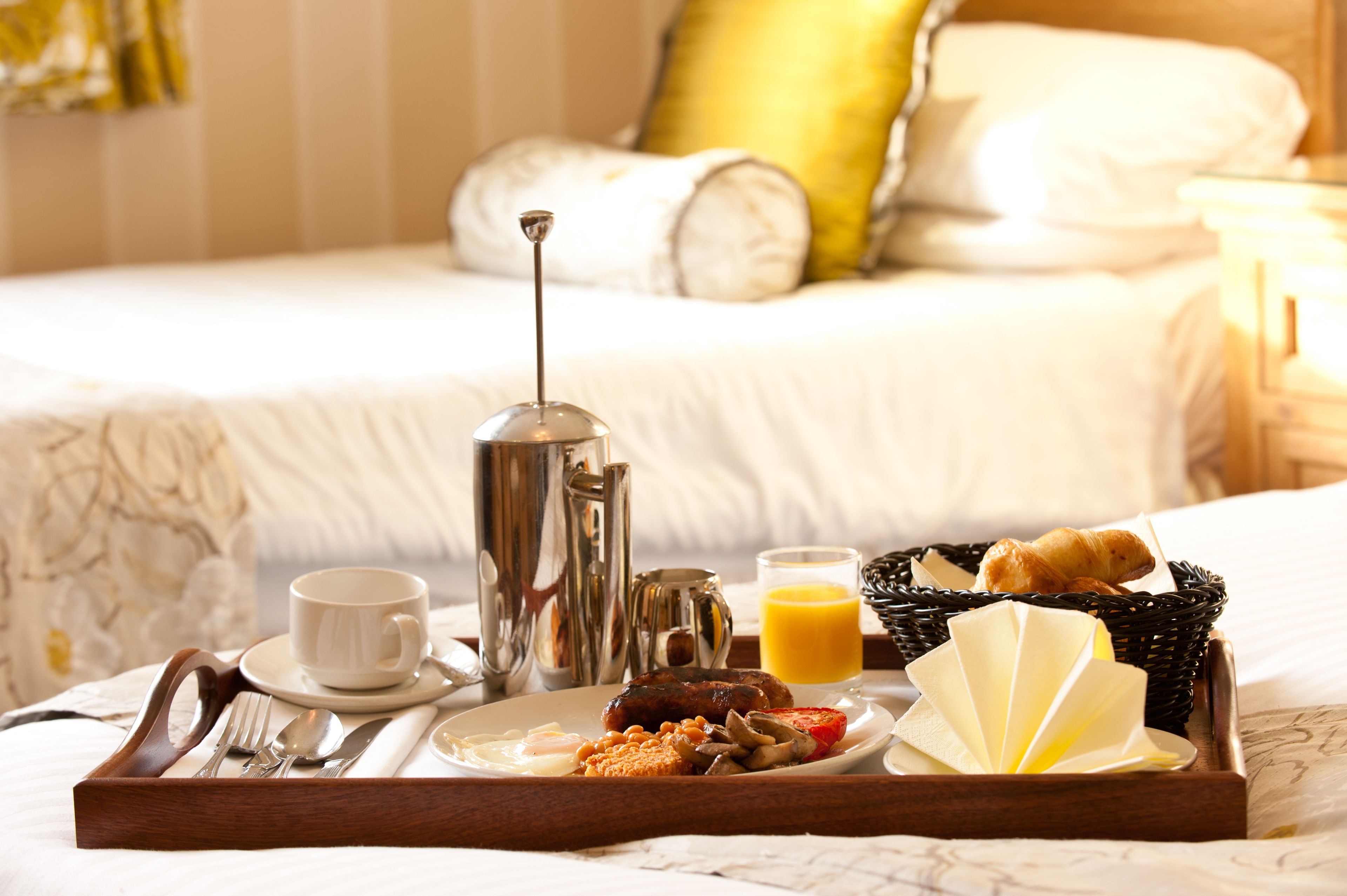Ein Frühstücksbrett mit Eiern, Würstchen, Toast und Saft in einem Hotelzimmer.