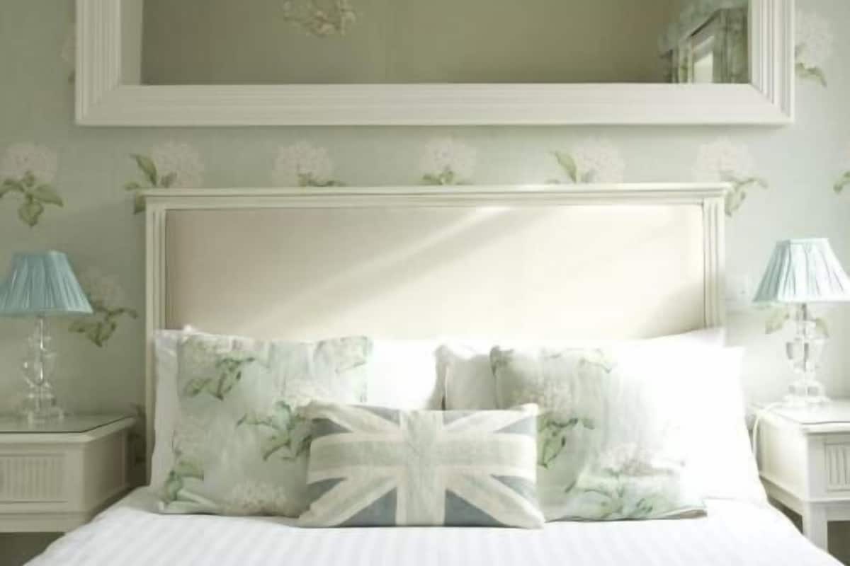 A bedroom with a bed, a nightstand, a lamp, a mirror, and a floral wall design.