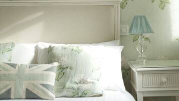 A bed with floral bedding and a Union Jack pillow, a bedside lamp, and a nightstand with a mirror.