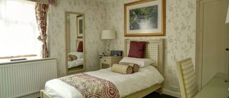 A bedroom with a bed, bedside table, lamp, and a painting on the wall.