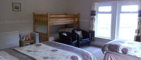 A bedroom with two beds, a bunk bed, a chair, and a window.