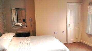 A bedroom with a bed, a mirror, a door, and a light switch.