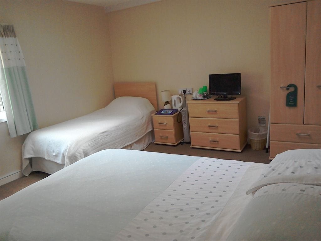 Habitación de hotel con dos camas, un escritorio con computadora, un armario y un pequeño cesto de basura.