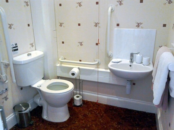 Un baño con inodoro, bidé, lavamanos y barras de apoyo.