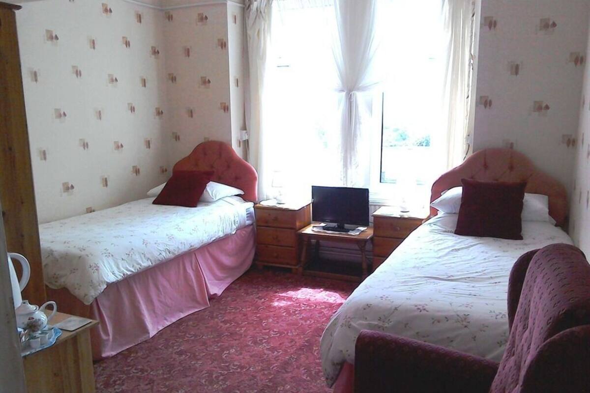 A room with two single beds, a wooden nightstand with a lamp, and a small table with a laptop.