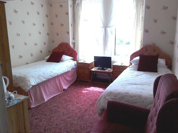 A room with two single beds, a wooden nightstand with a lamp, and a small table with a laptop. - Harepath Holidays Limited (Seaton)