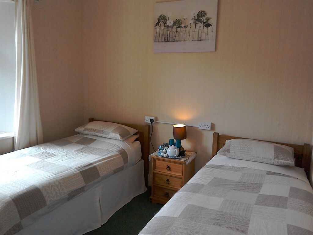 Et hotelværelse med to senge, et sengebord med lampe, et billede på væggen og et vindue med gardiner.