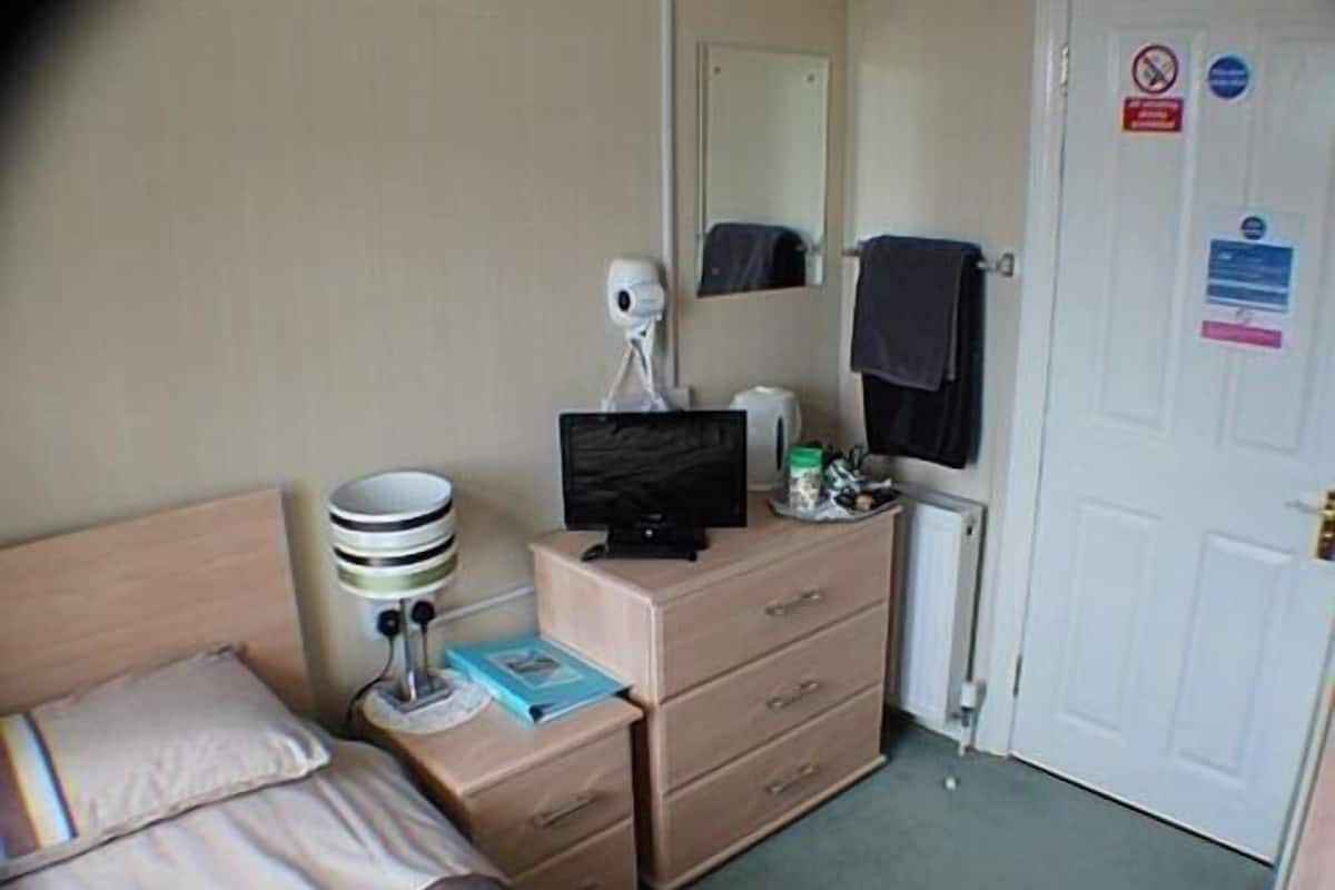 A hotel room with a bed, a desk with a computer, a mirror, a radiator, and a door with a no-smoking sign.