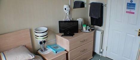 Ett hotellrum med en säng, ett skrivbord med en dator, en spegel, ett element och en dörr med en skylt som förbjuder rökning.