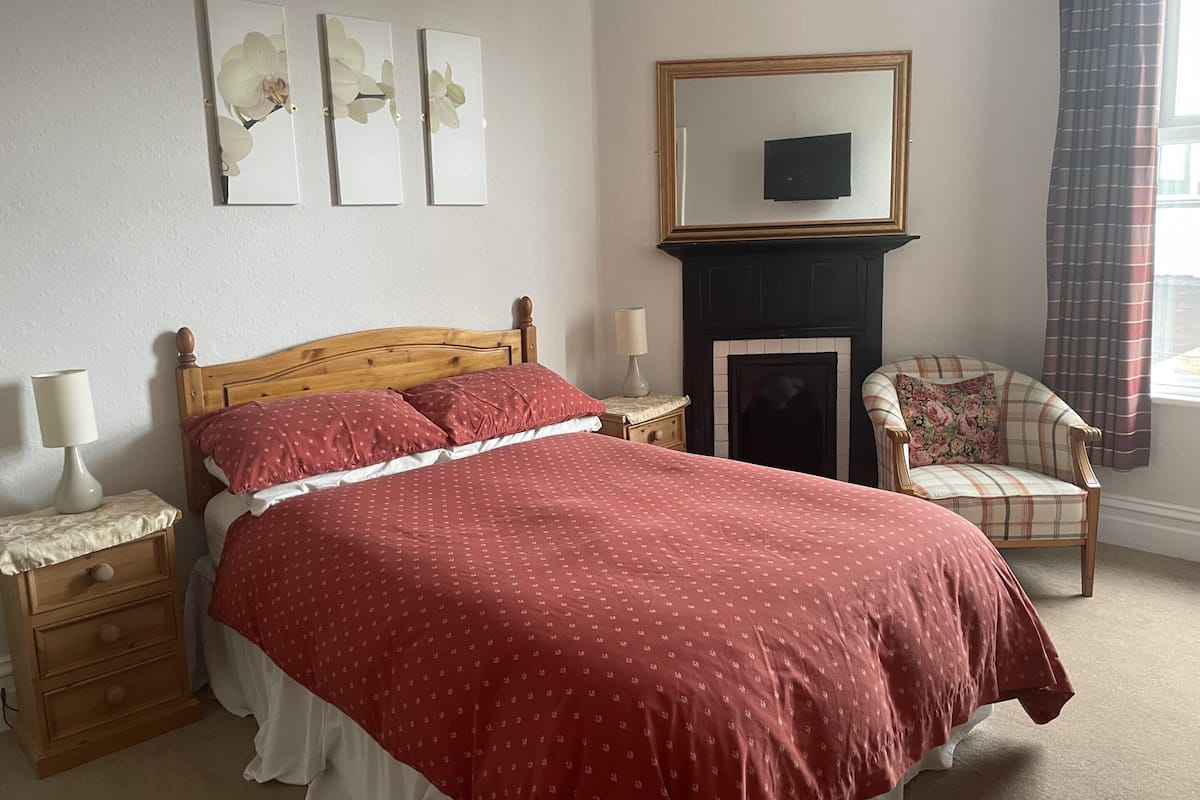 Een slaapkamer met een houten bed, twee nachtkastjes met lampen, een stoel, een open haard en wanddecoratie.