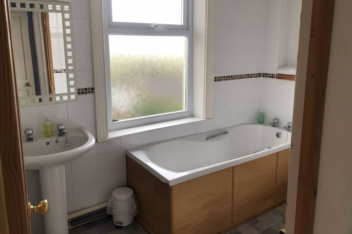 Een badkamer met een witte wastafel, een spiegel, een raam, een badkuip en houten kastjes.