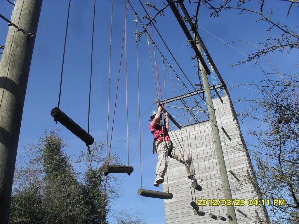 A person navigating an outdoor obstacle course with ropes and wooden beams.
