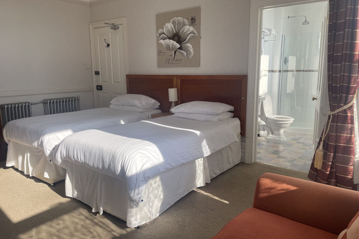 Hotelkamer met twee bedden, een radiator, een douchegedeelte en een deur met een handgreep.