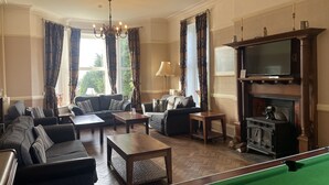 Ein Wohnzimmer mit einer Sofagarnitur, einem Couchtisch, einem Billardtisch, einem Kamin und einem Fernseher.