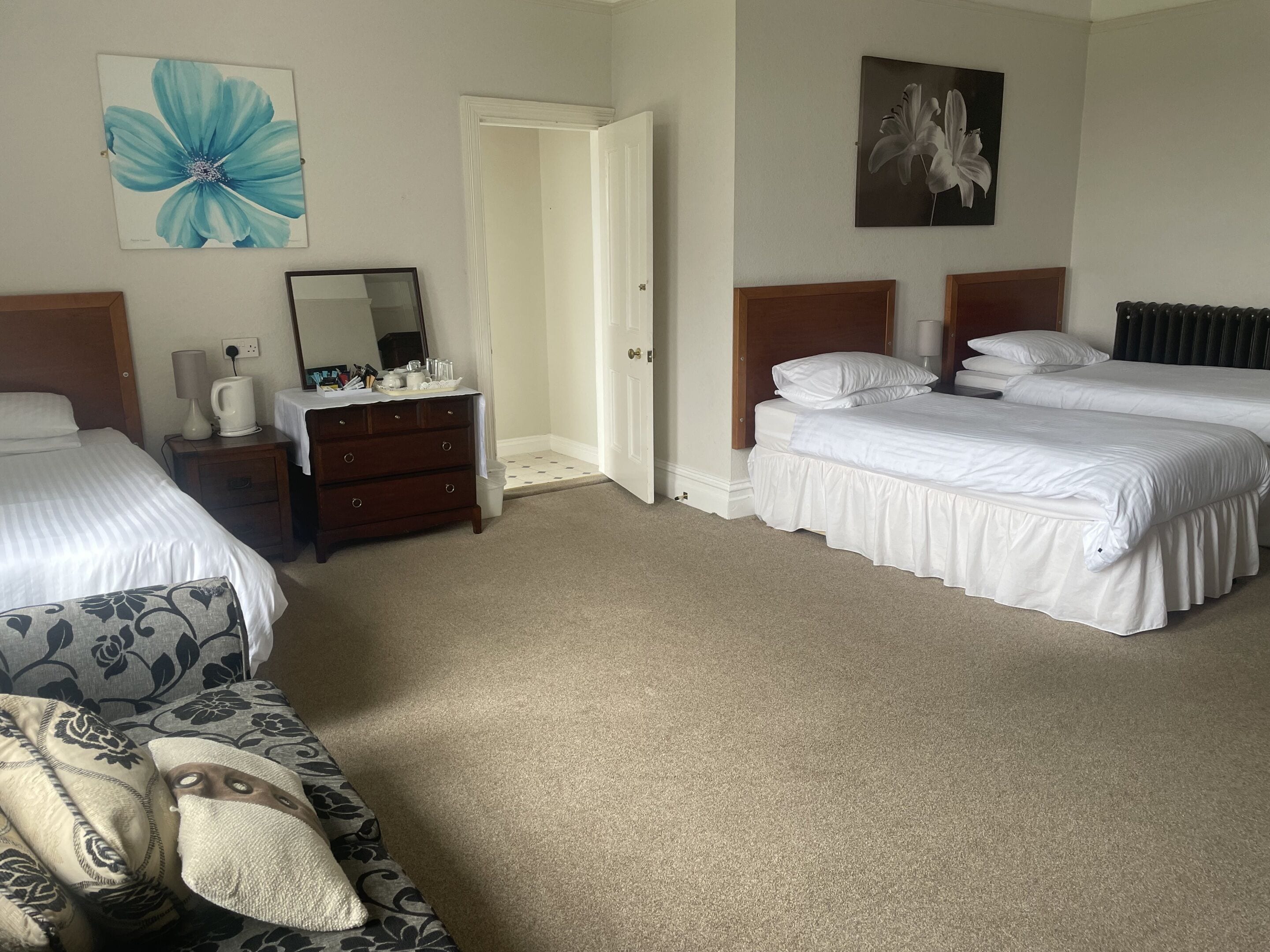 A hotel room with two beds, a dresser, a chair, and a door leading to another room.