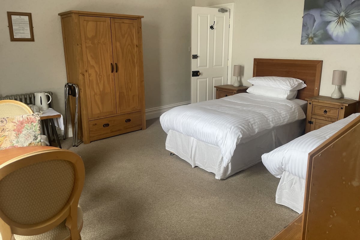 Een slaapkamer met een bed, nachtkastjes, een houten garderobe, een stoel en een radiator.