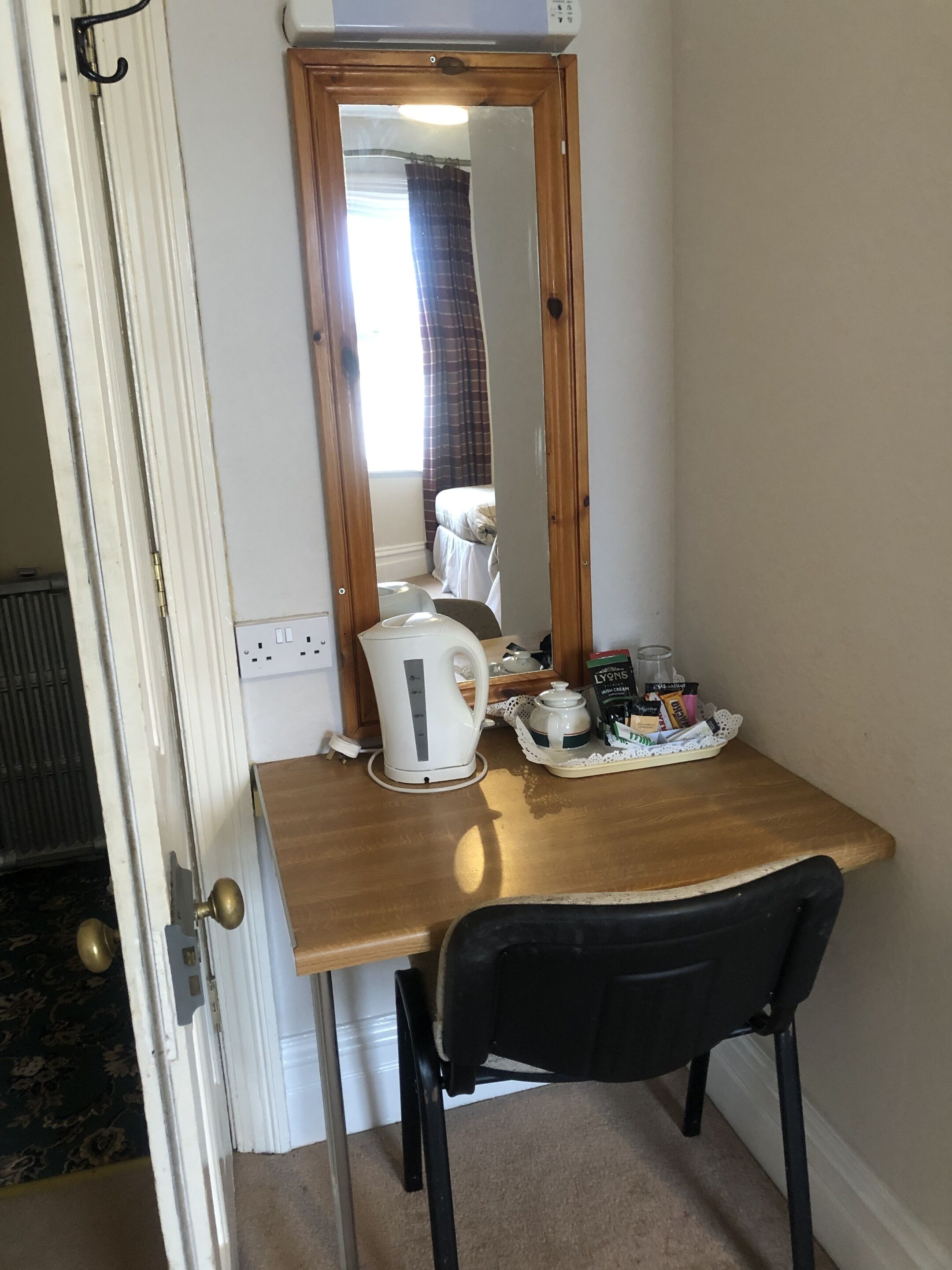 A small room with a wooden desk, a black chair, a white kettle, and a tray with coffee and tea products.