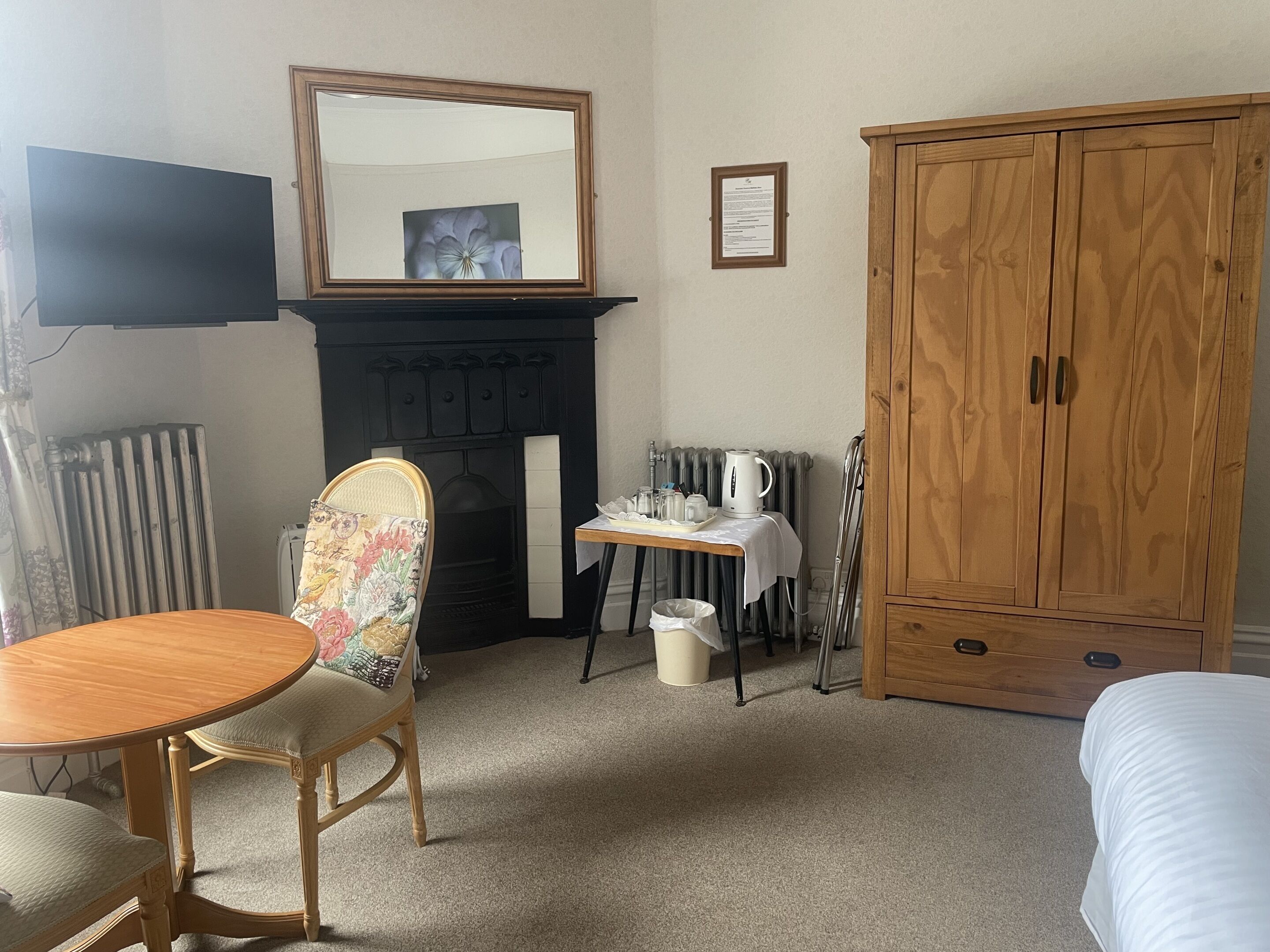 A room with a wooden chair, a table, a fireplace, a wooden wardrobe, and a radiator.