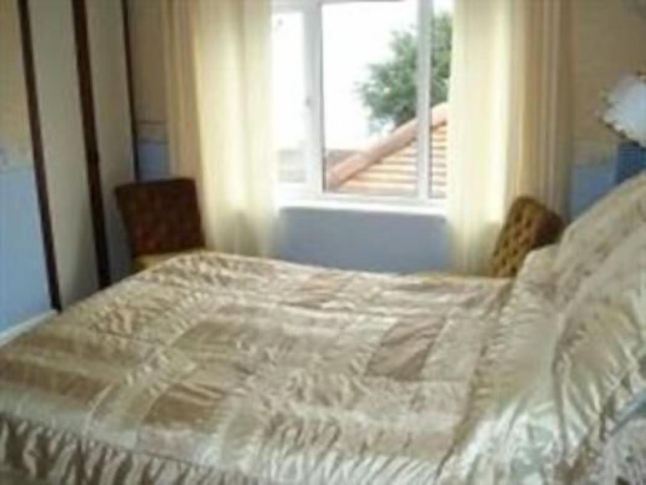 A bedroom with a bed, a window, and a chair.