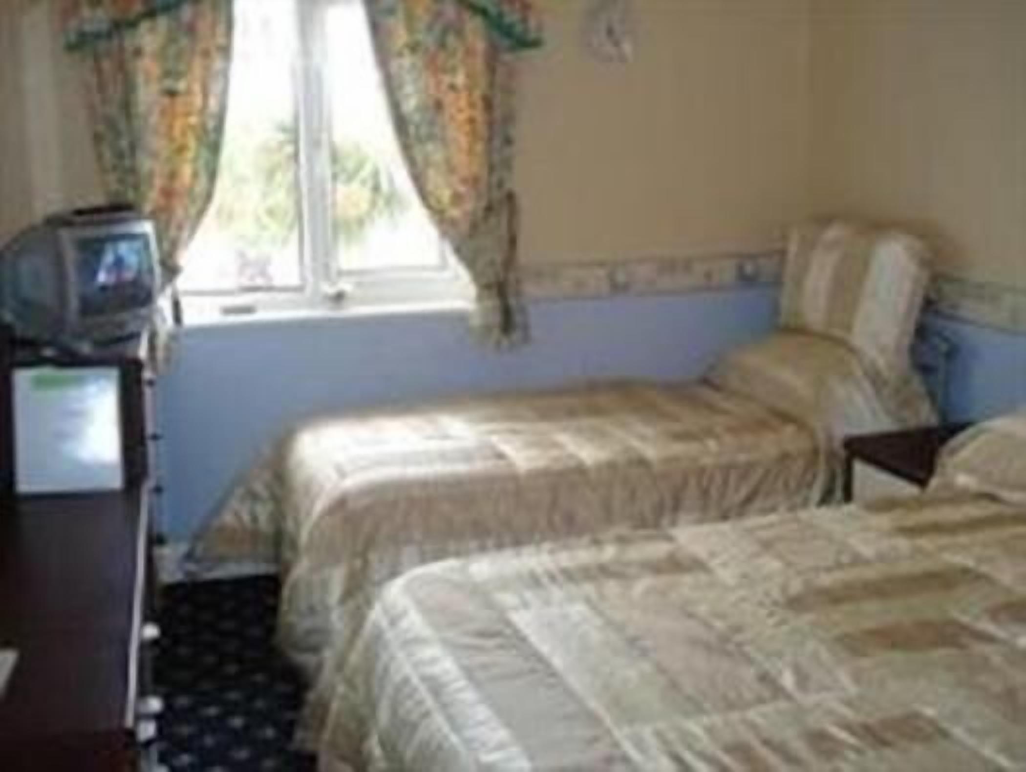 Une chambre avec deux lits, une petite table avec un téléviseur et une fenêtre avec des rideaux.