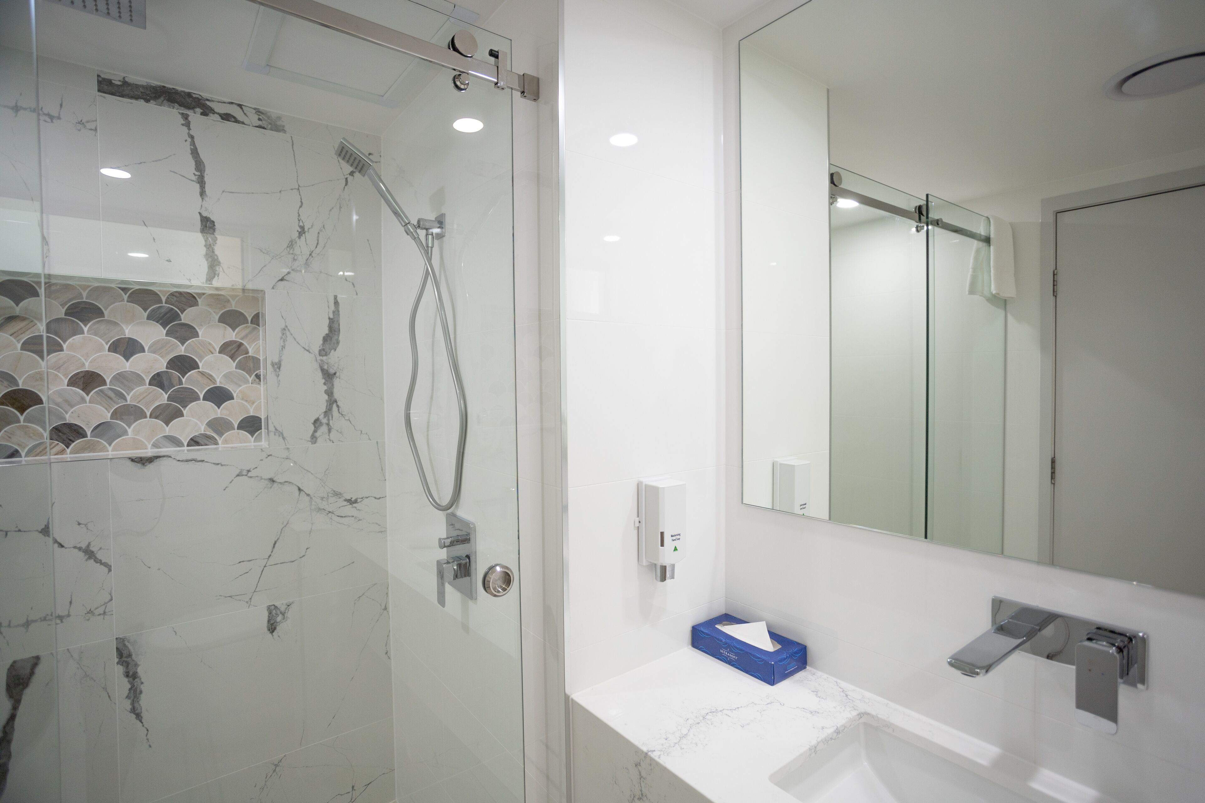 A modern bathroom with a glass-enclosed shower, a white sink with a marble countertop, and a large mirror.