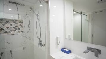 A modern bathroom with a glass-enclosed shower, a white sink with a marble countertop, and a large mirror.