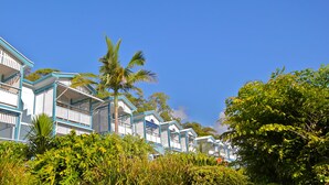 A row of blue and white beachfront villas with balconies, surrounded by lush greenery and palm trees. - Tangalooma Island Resort (Moreton Island)