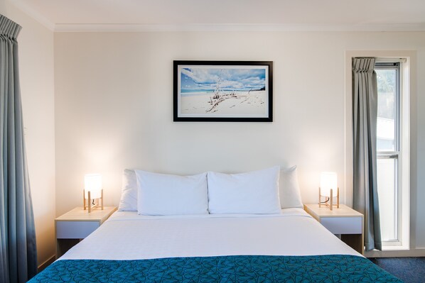 Una habitación de hotel con una cama grande, dos mesitas de noche con lámparas, un cuadro en la pared y una ventana con cortinas.