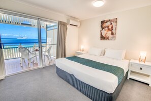A hotel room with a balcony, a bed with white and teal bedding, a nightstand with a lamp, and a wall-mounted artwork. - Tangalooma Island Resort (Moreton Island)